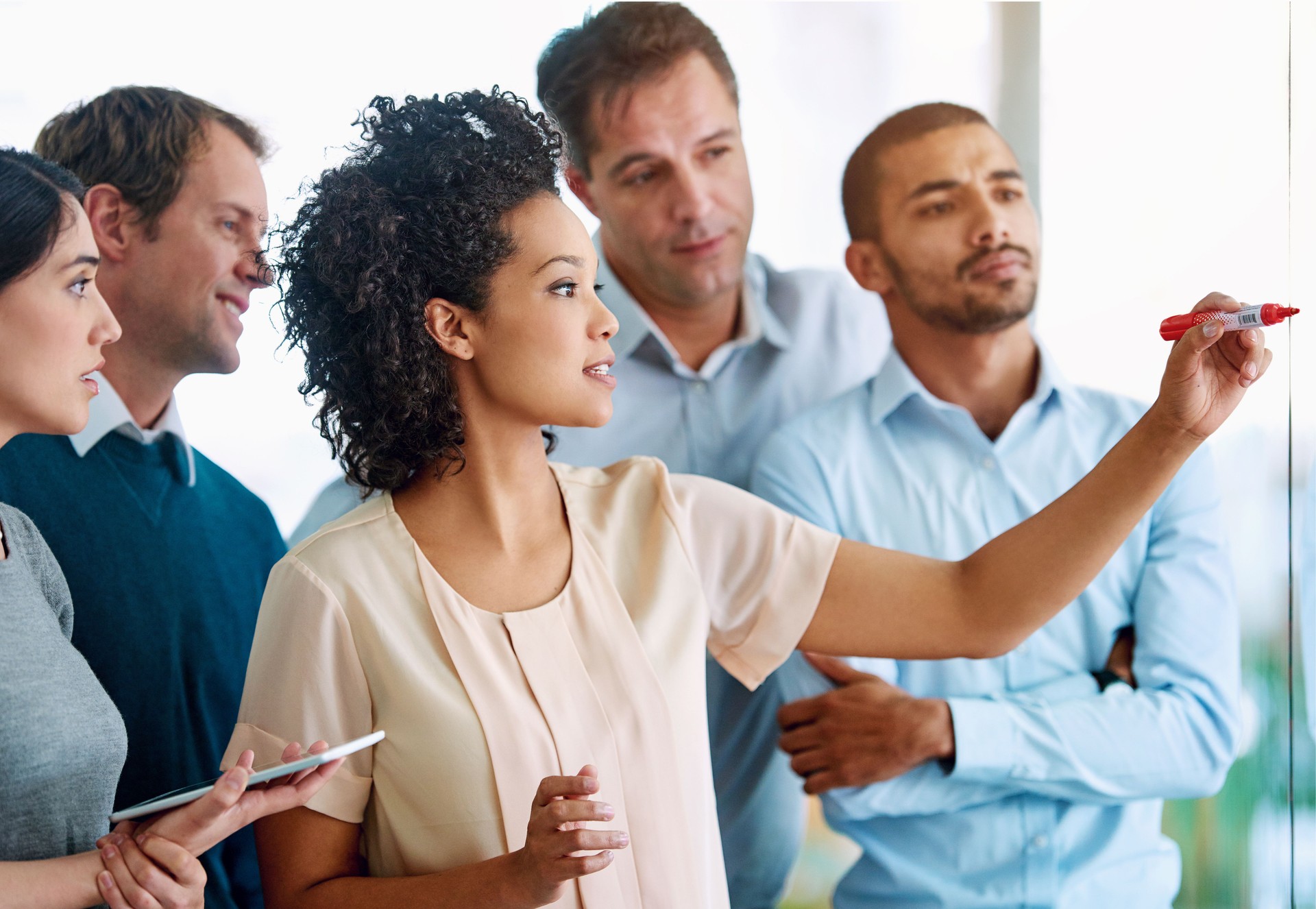 Business people, writing and coaching with tablet for planning, tasks or agenda on glass board at office. Group of young and creative employees taking notes for discussion, brainstorming or startup