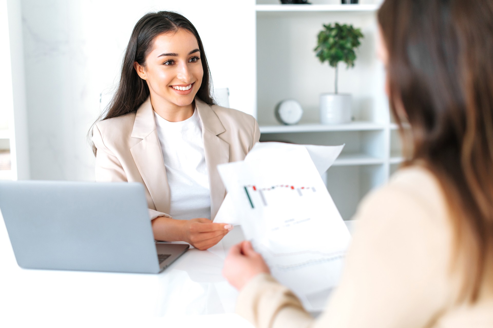 Teamwork. Two successful female colleagues are sitting at a desk, discuss financial strategy in modern office, analyzing financial report, planning business plan, smile.Brainstorm, partnership concept